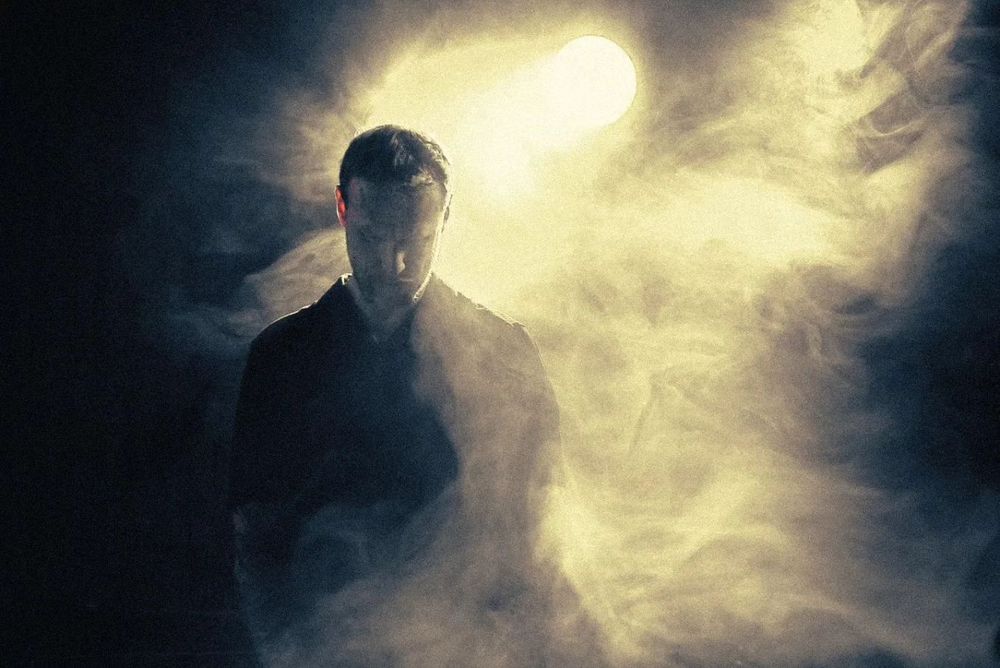 Host standing in smoke under a bright overhead light